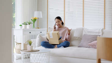 Upset mad asia people young girl consumer sit sofa at home open fake product order, damage post mail buy from online shopping retail store. Shock sad teen woman unbox from wrong bad shipping service.の写真素材