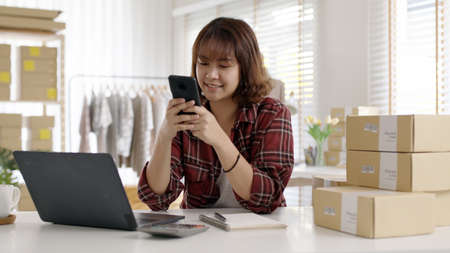 Young asia seller woman happy work on laptop busy cellphone call chat to customer at home office desk use digital tablet computer in SME online store social e-commerce sale page service web support.の写真素材