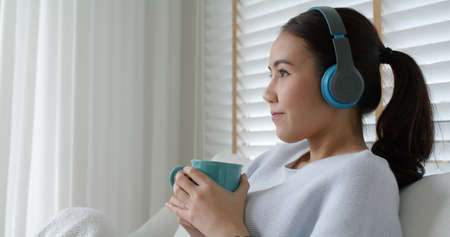Asia teen girl people enjoy coffee in break time self relax happy joy with good song in online radio app sitting rest sleep at cozy sofa. Youth fun hobby indoor lazy zen life smile napping at home.の写真素材