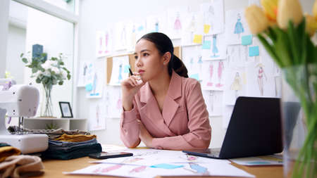 Woman seller SME retail store owner work hard worry stress in bad news on laptop at home office desk. Asian people crisis tailor job issue feel tired tough and upset in cash money loss or loan debt.の写真素材