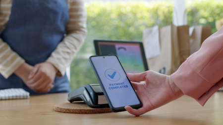 Close-up hand asia woman people work in small sme coffee cafe shop store owner use cashless wifi paywave nfc scan app smart pos reader sale in take out food drink order in urban city life contactless.の写真素材