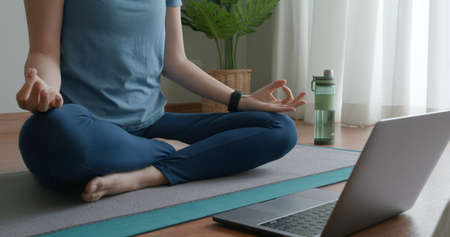 Close-up asia people woman enjoy study happy watch live video sit on sport mat at cozy home floor indoor easy zen class. Body calm life stress relax asana lotus pose in laptop self learn online media.の写真素材