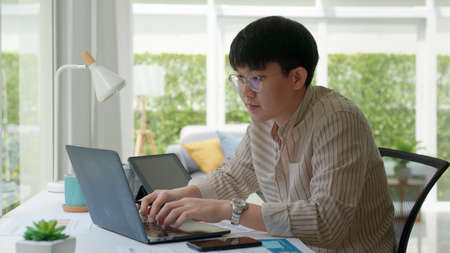 Asia people happy man coding on laptop work remotely at home office sit relax smile write e-mail search data on desk. MBA online study class in reskill upskill college learning for job career path.の写真素材