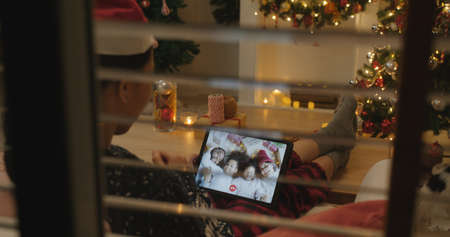 X'mas asia happy woman relax smile laugh greet in digital tablet screen remote talk to child kid friend at night online video VoIP party sit on cozy sofa at home enjoy good warm time winter season.の写真素材