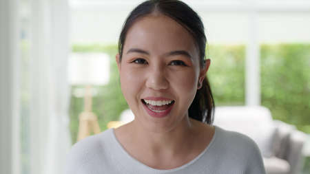 face selfie screen of asia people look at camera waving hand greeting sit relax at home sofa enjoy talk laugh sharing on social media online dating. Lady blogger shoot video VoIP create content.の写真素材
