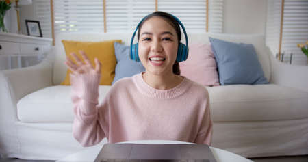 face selfie screen of asia people look at camera waving hand greeting sit relax at home sofa enjoy talk laugh sharing on social media online dating. Lady blogger shoot video VoIP create content.の写真素材
