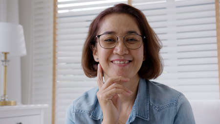 Close-up asia older aging parent or latin lady toothy smile laugh sitting carefree easy on sofa couch in house in early retired teacher wisdom life for people aged 40S, 50S or 60S consumerism concept.の写真素材