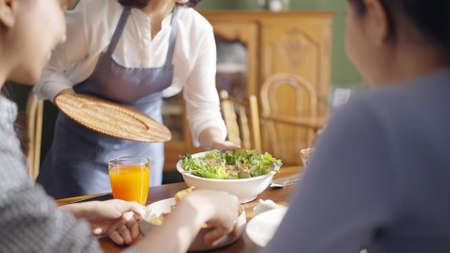Adult SME owner work at busy small cafe bar pub on cozy day carry plate tray for group asia people friend party at vegan shop. Enjoy talk order fresh menu eat meal drink fine dish diet salad bowl.の写真素材