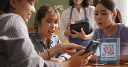 Adult waiter staff casual apron SME owner enjoy work listen to young asia people smile fun talk look at smart QR code on mobile app eat vegan meal after reopen coffee shop food drink inside cafe bar.の写真素材