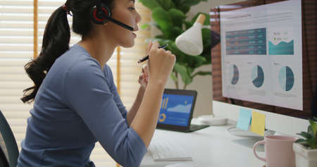 Asia people young casual woman remote work at desk home phone call talk study learn MBA online class. SEO sale plan report data chart graph on desktop PC screen reskill upskill career job workforce.の写真素材