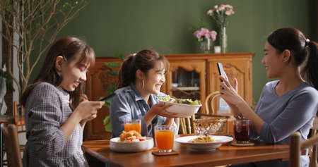 Small girl group party asia people busy talk smile eat brunch food drink. Young woman fun happy hour meal shoot photo of dish plate salad bowl on table post ig reel story app in vegan cafe bar shop.の写真素材
