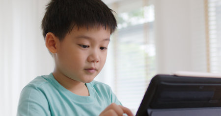 Cute asia people alpha Gen Z kid small boy happy play video game app online at home. Enjoy fun class little child care study learn upskill idea course look at touch screen smart tech digital tablet.の写真素材