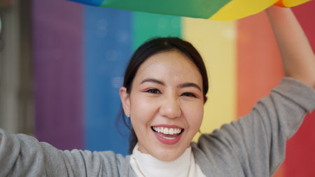 Portrait young teen queer transgender asia people playful dance waving colorful stripes flag fun smile laugh. Proud of LGBT or LGBTQIA culture sign bisexual festival march parade at city street town.の写真素材