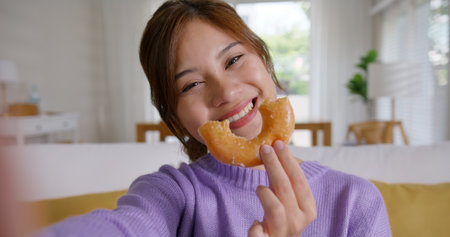 Young vlogger asia people influencer girl take photo eat bite smiley donut funny face post review on instagram tiktok reel app. Sweet tooth food sugar lover enjoy fun show viral video camera at home.の写真素材