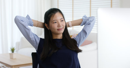Asia people workforce young woman remote work at home office sit easy relax enjoy break time life balance put hands behind head and lean back on cozy desk. Teen girl stress relief look at desktop PC.の写真素材
