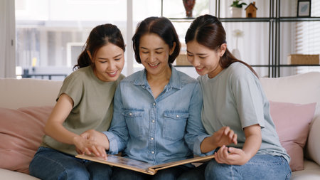 Recall the past life memories Happy time Mother's day grown up kid child joy fun look at old retro photo album with mature mum. Asia adult people middle age mom smile enjoy relax sitting at home sofa.の写真素材
