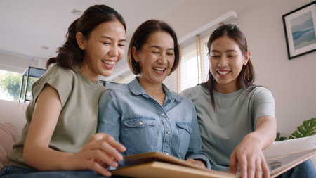 Recall the past life memories Happy time Mother's day grown up kid child joy fun look at old retro photo album with mature mum. Asia adult people middle age mom smile enjoy relax sitting at home sofa.の写真素材