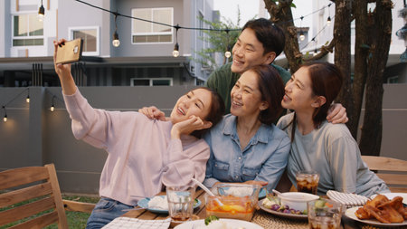 Young adult asia people hug love care for mom taking photo selfie video on mobile phone camera at home picnic dining fun night party dine table. Relax older mum smile enjoy warm time happy hour meal.の写真素材