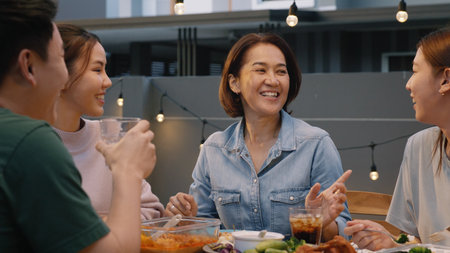 Middle aged mom fun talk smile at dine table home party. Asia people adult old mum enjoy food joy laugh happy hour at cozy picnic warm time on night meal weekend day. Young senior woman relax retired.の写真素材
