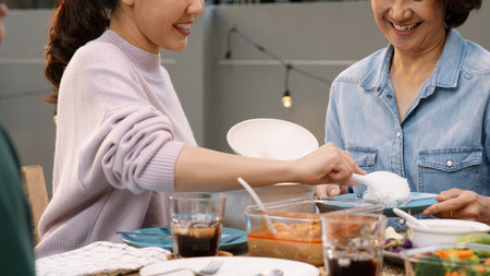 Love care giver Mother's day share serve scoop rice pass for middle age mum at home patio dine table party. Group of young asia people enjoy warm time eat thai picnic meal to adult parent mature mom.の写真素材