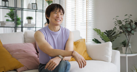 Gay queer asian man non-binary influencer sitting easy at home sofa. Asia non binary LGBT young guy adult two people happy relax smile talking asking advice face to face in mental health care therapy.の写真素材