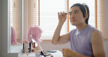 Gay queer man non-binary beauty blogger makeup artist at home cross dressing up apply face skin care...