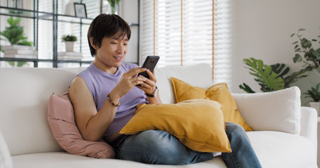 Gen Z queer man non-binary sitting easy relax happy read news on web page app at home sofa. Asia people LGBT young adult guy play web3, store shop e-commerce buyer, virtual retail network cyber payingの写真素材