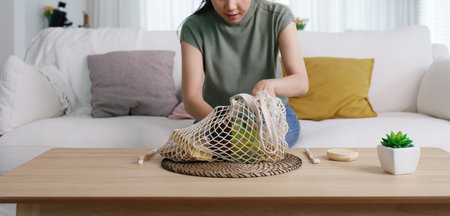 Young Gen Z girl asia people sit at home sofa couch unpack reuse mesh bag buy from eco friendly...