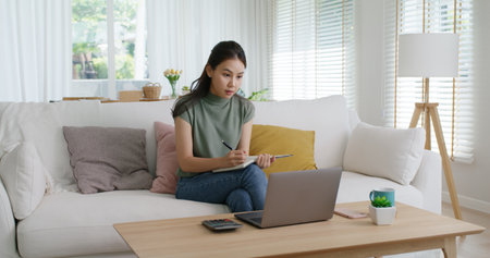Reskill upskill for young adult talent workforce remote work at home hybrid workplace. Asia woman happy smile sit at sofa couch learn online study MBA video call share plan idea write note on tablet.の写真素材