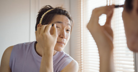 Gay queer man non-binary beauty blogger makeup artist at home cross dressing up apply face skin care eye make up brush. Real asia LGBT young guy adult people happy relax smile looking at mirror pride.の写真素材