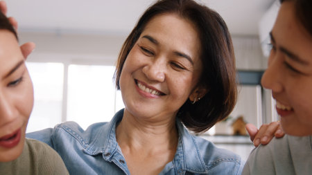 Middle aged mom smile look at two grown up kid child relax hug cuddle stroking with love care warm time. Asia people woman adult older mum parent sitting at home sofa sweet trust moment happy life.の写真素材