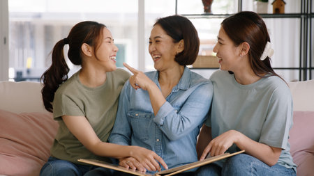 Recall the past life memories Happy time Mother's day grown up kid child joy fun look at old retro photo album with mature mum. Asia adult people middle age mom smile enjoy relax sitting at home sofa.の写真素材