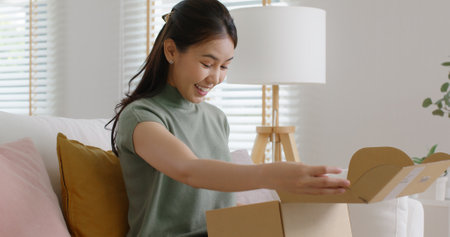 Young happy asia people teen girl smile enjoy unbox post mail sit relax at home comfort sofa couch feel joy amazed awe wow in omni channel fast send parcel via online sale shop store e-commerce order.の写真素材
