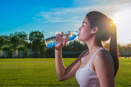 Young woman relaxing and drinking water from plastic bottles after jogging. Girl quenches thirst after fitness outdoors. Healthy lifestyle.の写真素材