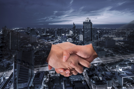 Double Exposure of a businessman handshake on blue tone Aerial view of cityscape Bangkok business district at twilight  background.の写真素材