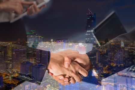 Double Exposure of a businessman handshake on bangkok cityscape in business district with high building at nightの写真素材