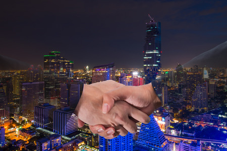 Double Exposure of a businessman handshake on bangkok cityscape in business district with high building at nightの写真素材