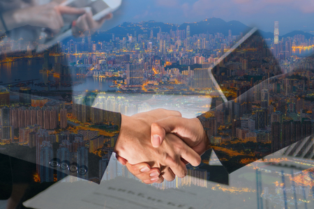 Double Exposure of a businessman handshake on Aerial view of Hong Kong cityscapeの写真素材