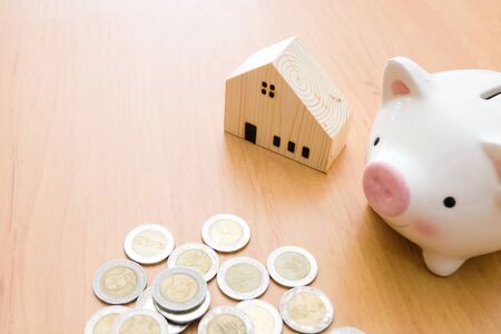 Selective focus of Piggy bank and wooden house on wood table with money coin.Saving plan to buy property, house. Personal financial concept for own a house. with copy space for textの写真素材