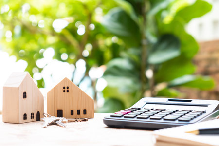 Selective focus at the wood house and calculator with iron key and notebook in foreground on wood table. With green leaf blurred background. Saving plan for home ownership concept.の写真素材