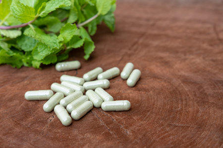 Selective focus at foreground of  medical green herb capsule with blurred fresh organic green herb leaf and capsule on wood background.  Medicine from nature, healthcare concept,の写真素材