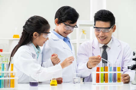 Young Asian boy and girl smile and having fun while doing science experiment in laboratory classroom with Teacher. Study with scientific equipment and tubes. Education concept.の写真素材