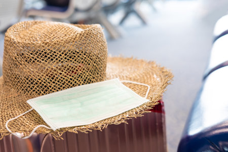 Defocus focus and blurred shot of surgical face mask, together with straw hat and travel luggage...
