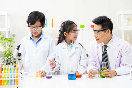 Young Asian boy and girl smile and having fun while learning science experiment in laboratory with teacher in classroom. Study with scientific equipment and tubes. Education concept.の写真素材