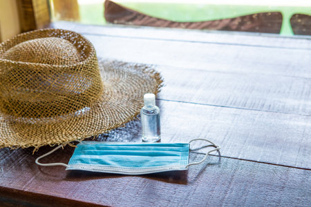 shot of surgical face mask, together with straw hat and on wooden table inside of the hotel. New normal lifestyle for traveler after Coronavirus.の写真素材