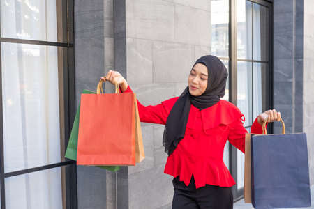 Beautiful East Asian Islamic women wearing hijab. Smile and feeling happy and holding many shopping bags walking in urban city area or department store. People lifestyle concept.の写真素材