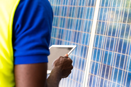 Selective focus at digital tablet. African men engineer inspect electrical solar panel and record information into mobile tablet. Alternative energy and industrial concept. Outdoor shot.の写真素材