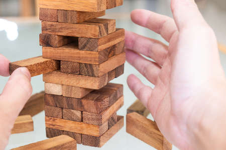Selective focus at wood brick. Business people using hand to pull out wood brick with caution. taking risk and make decision to play the game. Insurance or financial risk management and safety conceptの写真素材