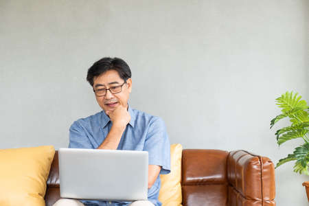 Selective focus at Old Asian men sit on the couch, having difficulty and  problem with internet and laptop computer.  Elder learning new technology or eye sight health issue.の写真素材
