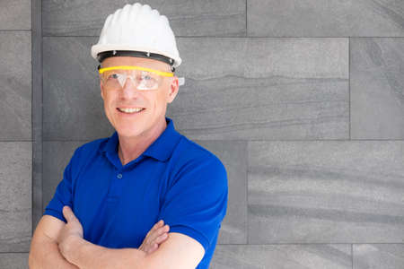 Selective focus at face of Caucasian foreman at building construction site, wearing protective hat and safety equipment while using digital tablet to record information. Civil engineer working.の写真素材